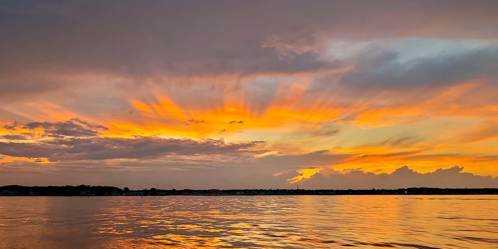 Photo of sunset behind clouds with a colorfuol sky over water